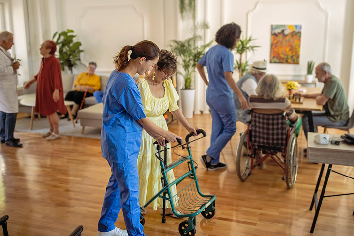 A caregiver assisting a resident with a walker in a senior living community common area